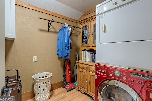 clothes washing area featuring stacked washer and dryer, cabinets, a textured ceiling, and light wood-type flooring