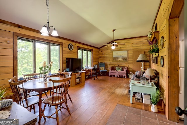 dining room featuring hardwood / wood-style floors, ceiling fan with notable chandelier, vaulted ceiling, and wooden walls