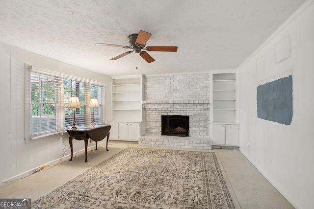 carpeted living room featuring built in shelves, ceiling fan, a brick fireplace, crown molding, and a textured ceiling