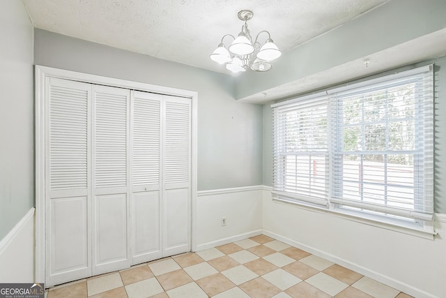 unfurnished bedroom with a notable chandelier, a textured ceiling, and a closet