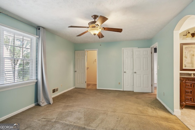 unfurnished bedroom with a textured ceiling, ceiling fan, light carpet, and connected bathroom