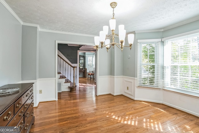 unfurnished dining area with a chandelier, wood-type flooring, a wealth of natural light, and ornamental molding