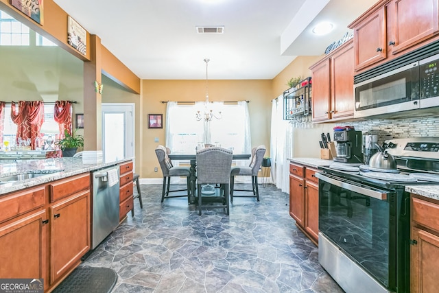 kitchen featuring light stone countertops, appliances with stainless steel finishes, backsplash, pendant lighting, and an inviting chandelier