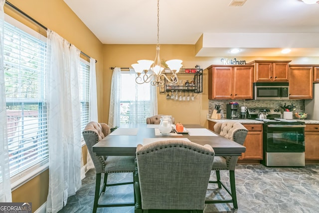 kitchen featuring appliances with stainless steel finishes, backsplash, a wealth of natural light, decorative light fixtures, and a notable chandelier