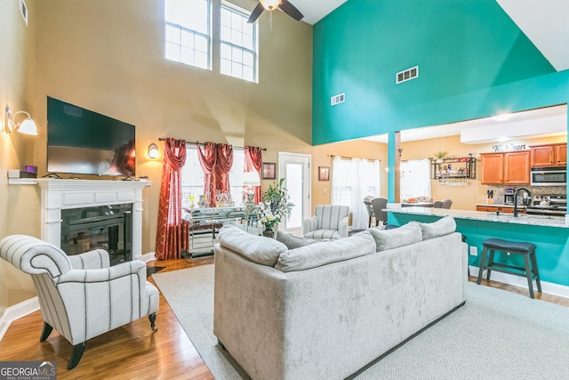 living room featuring a towering ceiling, light hardwood / wood-style floors, ceiling fan, and sink