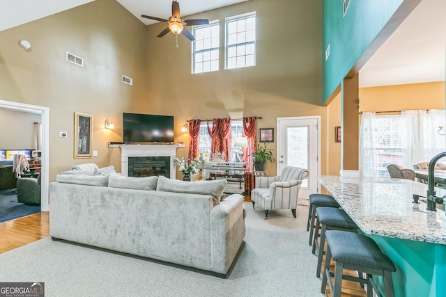 carpeted living room featuring ceiling fan, a towering ceiling, and a healthy amount of sunlight