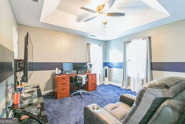 carpeted home office with a tray ceiling and ceiling fan