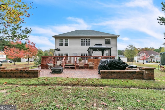 back of property featuring a lawn, a gazebo, a wooden deck, a patio area, and an outdoor fire pit