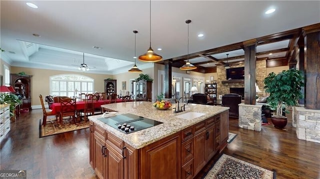 kitchen featuring sink, hanging light fixtures, a stone fireplace, dark hardwood / wood-style floors, and a center island with sink