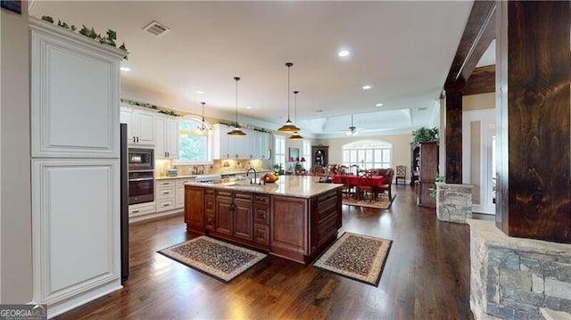 kitchen featuring sink, dark wood-type flooring, pendant lighting, a center island with sink, and white cabinets