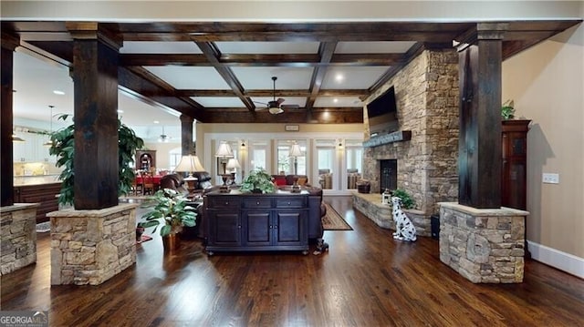 living room with ceiling fan, a stone fireplace, beamed ceiling, dark hardwood / wood-style floors, and decorative columns