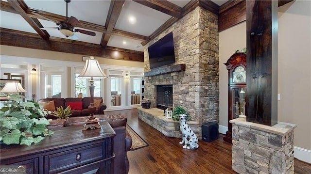 living room featuring ceiling fan, dark wood-type flooring, coffered ceiling, a stone fireplace, and beamed ceiling