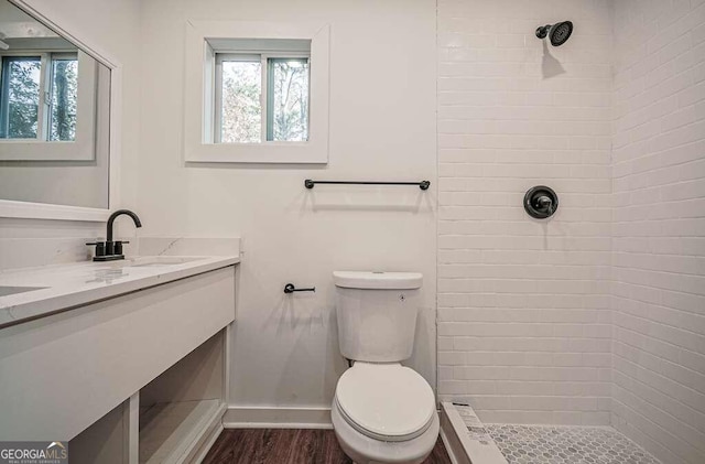 bathroom featuring tiled shower, vanity, hardwood / wood-style flooring, and toilet