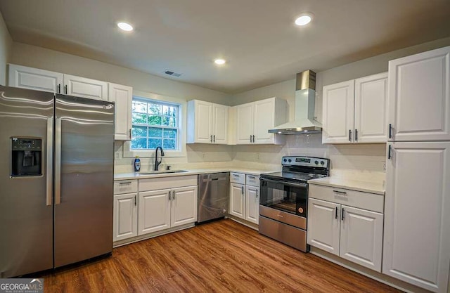 kitchen featuring wall chimney range hood, sink, hardwood / wood-style flooring, white cabinetry, and stainless steel appliances