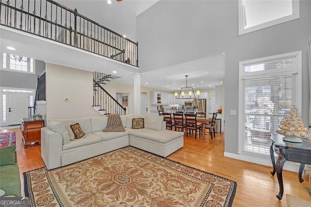 living area featuring stairway, wood finished floors, a high ceiling, ornate columns, and a chandelier