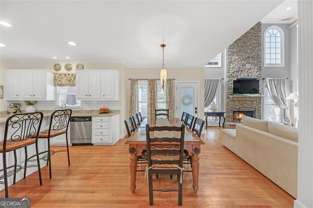 dining room with recessed lighting, a fireplace, a towering ceiling, and light wood finished floors