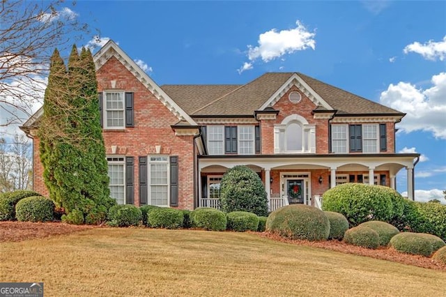 view of front facade featuring a porch, a front yard, and brick siding