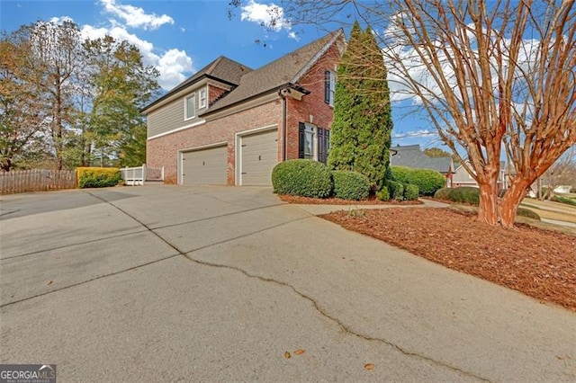 view of home's exterior with a garage, driveway, brick siding, and fence