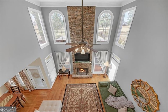 living area featuring crown molding, a towering ceiling, a ceiling fan, a large fireplace, and wood finished floors