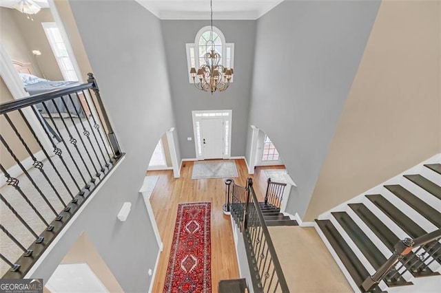 foyer entrance with light wood-type flooring, crown molding, a high ceiling, and a chandelier