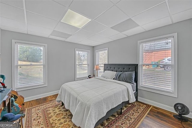 bedroom featuring baseboards, a drop ceiling, and wood finished floors