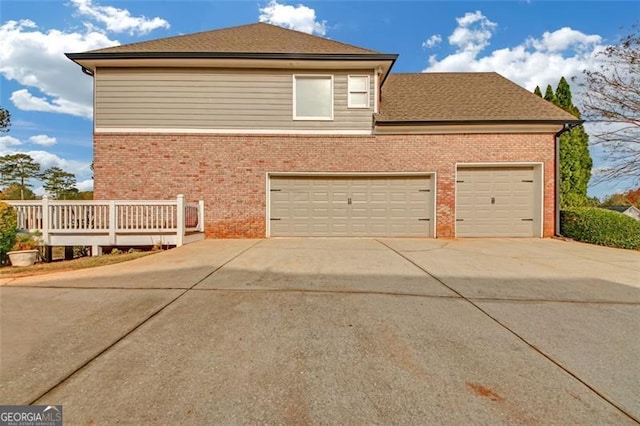 view of side of property featuring driveway, a shingled roof, a garage, and brick siding