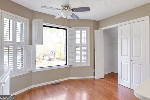 unfurnished bedroom featuring multiple windows, ceiling fan, wood-type flooring, and a textured ceiling