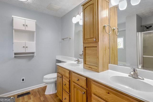 bathroom with vanity, a textured ceiling, hardwood / wood-style flooring, toilet, and a shower with shower door