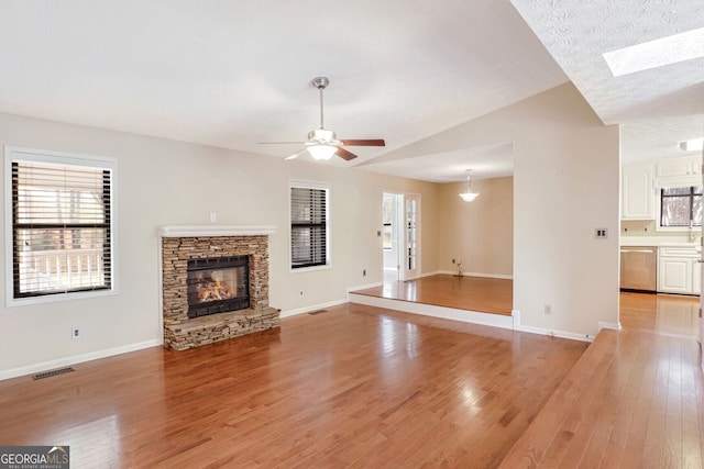 unfurnished living room featuring a fireplace, ceiling fan, light hardwood / wood-style flooring, and lofted ceiling with skylight