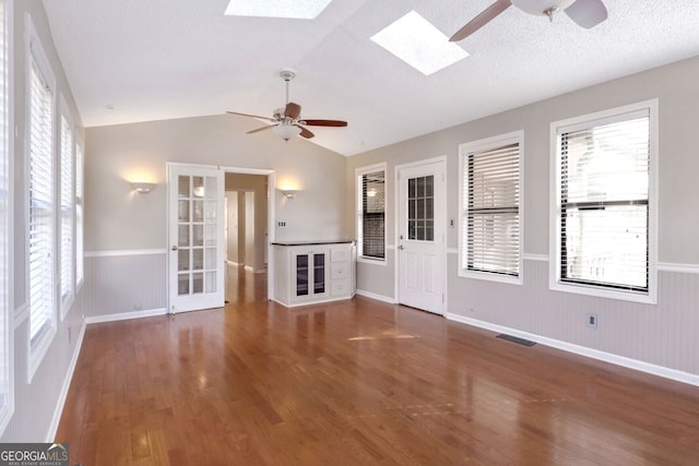 unfurnished living room featuring a textured ceiling, ceiling fan, lofted ceiling with skylight, and dark wood-type flooring