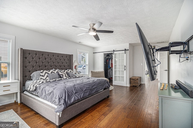 bedroom with dark wood-type flooring, ceiling fan, a barn door, a textured ceiling, and a closet