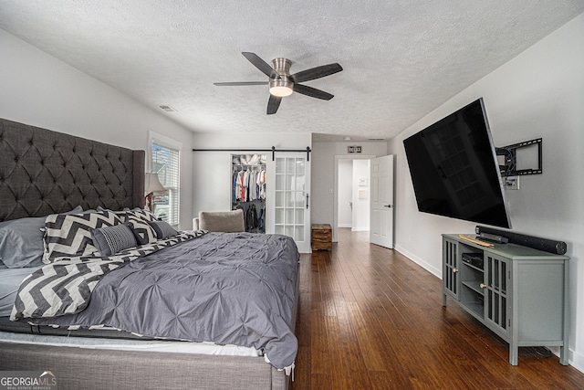 bedroom with dark hardwood / wood-style floors, ceiling fan, a barn door, a textured ceiling, and a closet