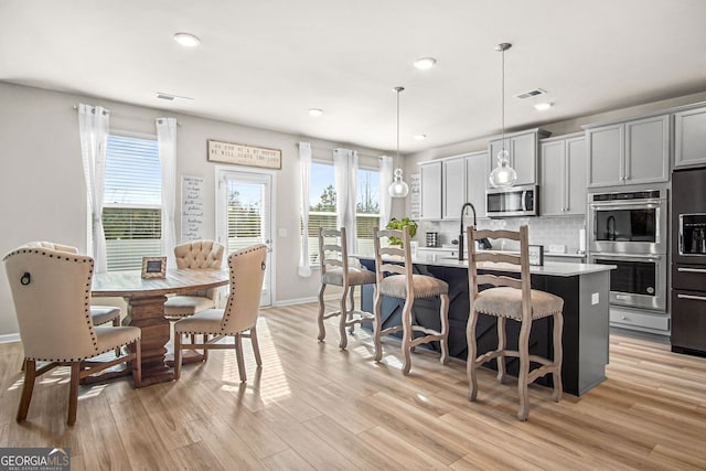 kitchen with pendant lighting, a kitchen island with sink, gray cabinets, appliances with stainless steel finishes, and tasteful backsplash