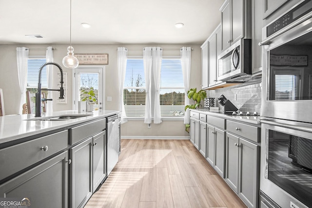 kitchen with gray cabinetry, pendant lighting, sink, and stainless steel appliances