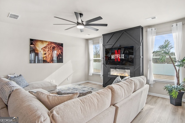 living room with ceiling fan, a fireplace, and light hardwood / wood-style floors