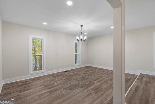 spare room with a chandelier and dark wood-type flooring