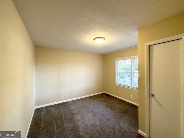 empty room featuring a textured ceiling and dark colored carpet