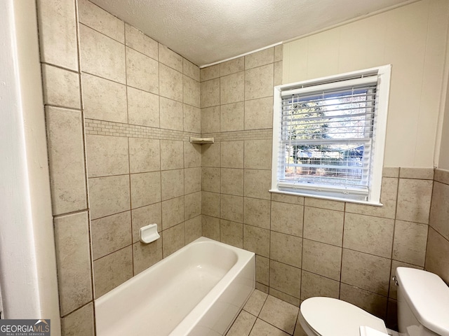 bathroom with a bathtub, tile patterned flooring, toilet, a textured ceiling, and tile walls