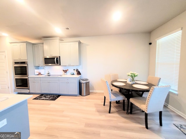 kitchen with appliances with stainless steel finishes, light countertops, light wood-type flooring, and baseboards