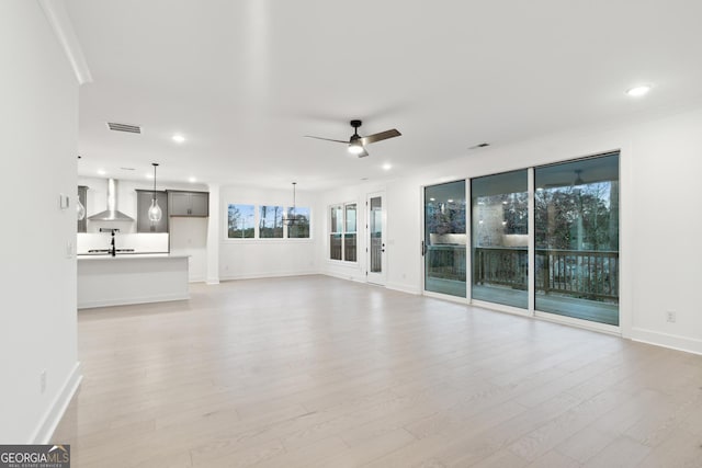 unfurnished living room featuring sink, light wood-type flooring, plenty of natural light, and ceiling fan