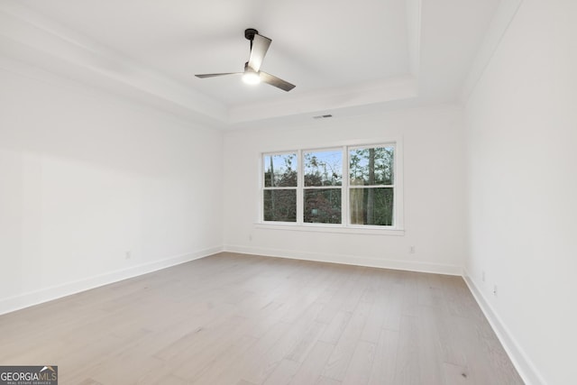 empty room with ceiling fan, a raised ceiling, ornamental molding, and light hardwood / wood-style flooring