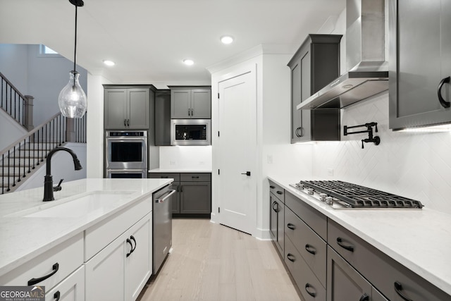 kitchen featuring wall chimney range hood, sink, appliances with stainless steel finishes, decorative light fixtures, and white cabinetry