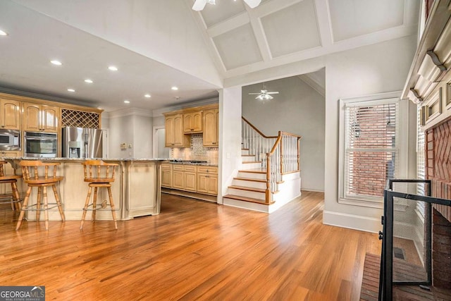 kitchen featuring appliances with stainless steel finishes, a breakfast bar, ceiling fan, light brown cabinets, and light hardwood / wood-style flooring