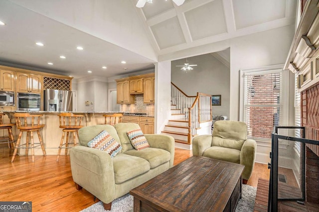 living room with ceiling fan, coffered ceiling, high vaulted ceiling, crown molding, and light wood-type flooring