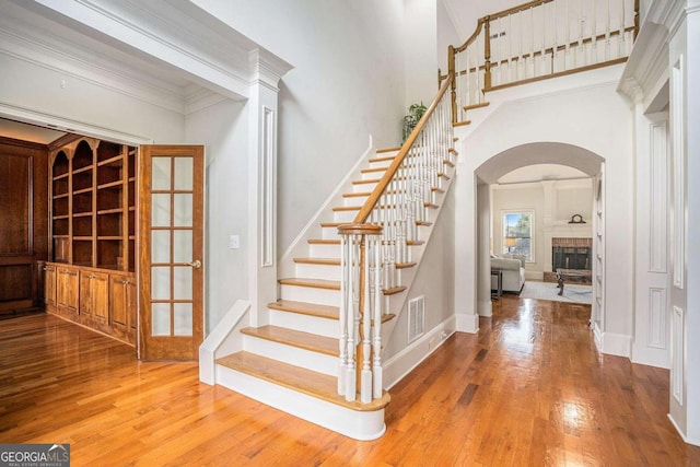 staircase with hardwood / wood-style flooring, a towering ceiling, and crown molding