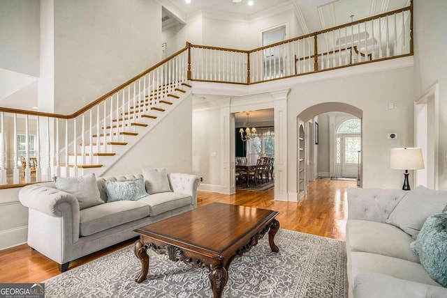 living room featuring a chandelier, a towering ceiling, light hardwood / wood-style flooring, and crown molding