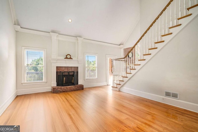 unfurnished living room featuring hardwood / wood-style floors, crown molding, and a brick fireplace