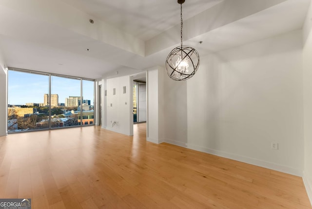 unfurnished room featuring hardwood / wood-style floors, a notable chandelier, and a wall of windows