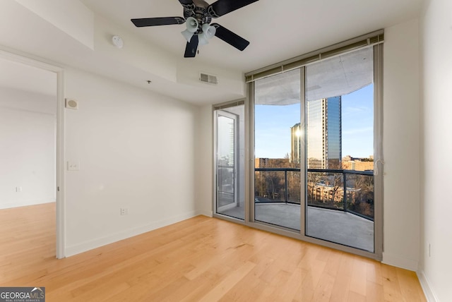 unfurnished room with hardwood / wood-style flooring, a wall of windows, and ceiling fan