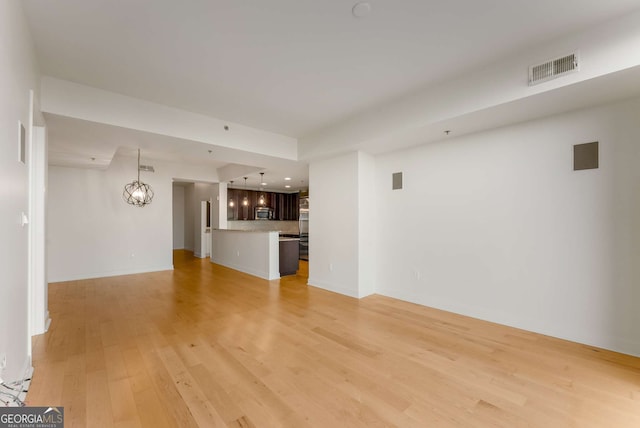 unfurnished living room featuring an inviting chandelier and light hardwood / wood-style flooring